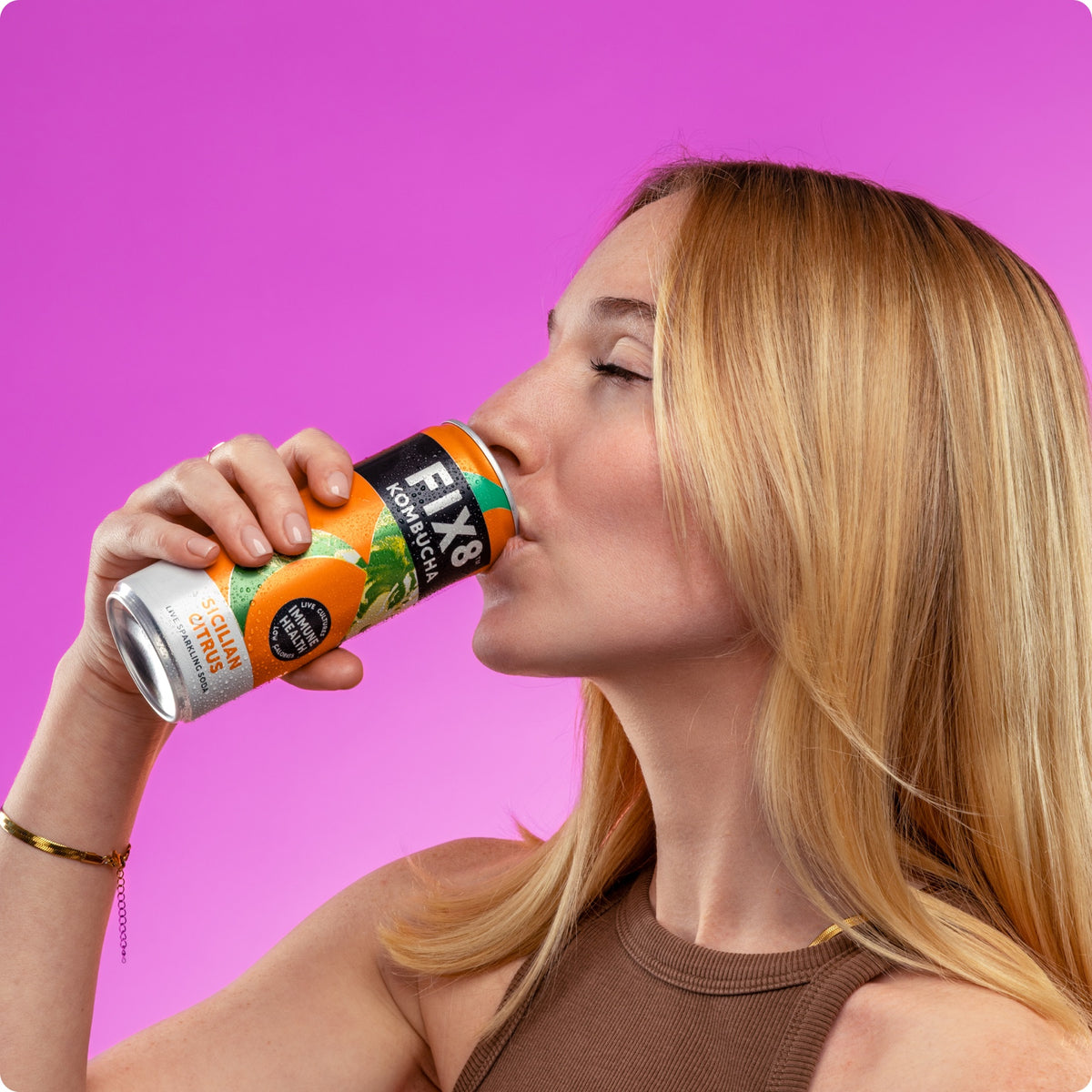 Woman drinking a can of Fix8 Sicilian Citrus kombucha against a pink background